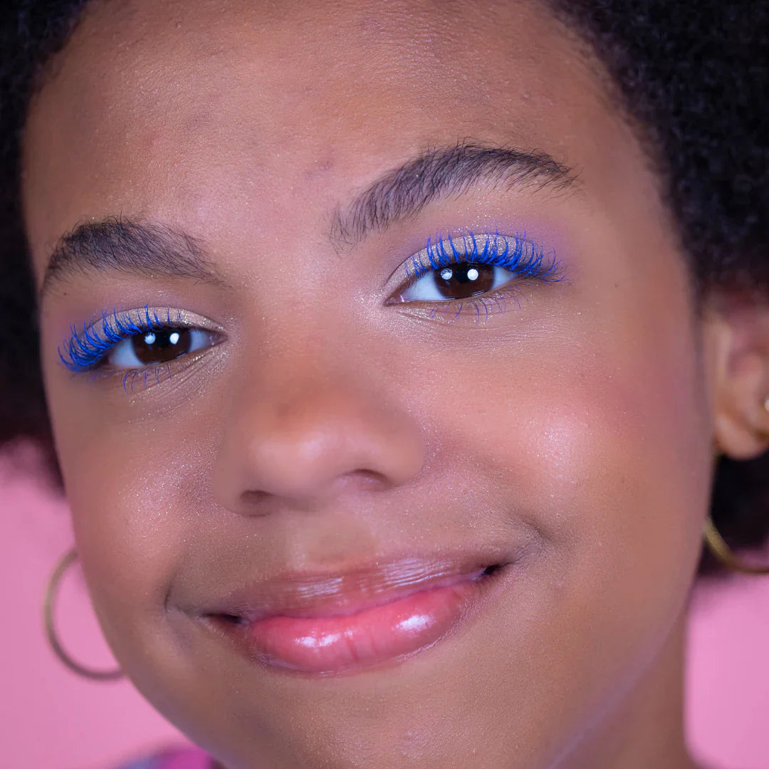 Model met helderblauwe Mascara Superheld van Camille op de wimpers, tegen een roze achtergrond
