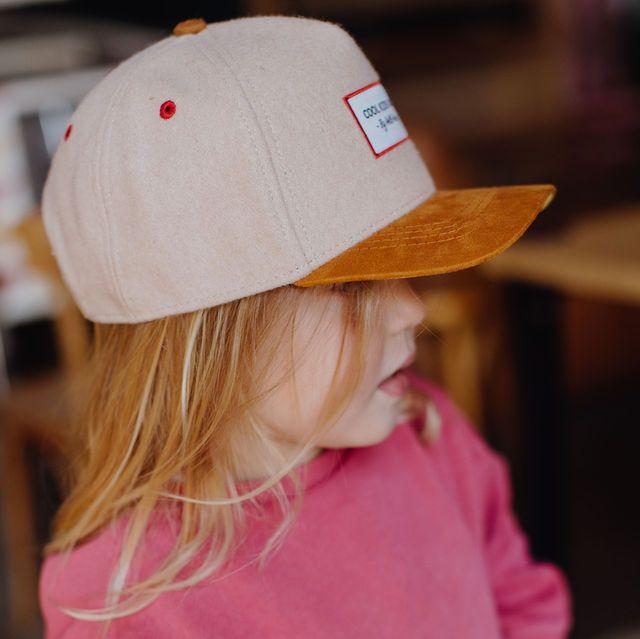 Zijaanzicht van een kind met de beige Melton Creamy pet met okerkleurige klep en rode ventilatiegaatjes.