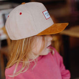 Zijaanzicht van een kind met de beige Melton Creamy pet met okerkleurige klep en rode ventilatiegaatjes.