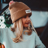 Kind met bruine Block Macaroon muts van Hello Hossy met roze pompon en lichtgroene trui, van opzij gezien.