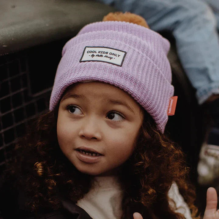 Kind kijkt opzij met de lila Hello Hossy Block Mauve muts met bruine pompon en omgeslagen rand.
