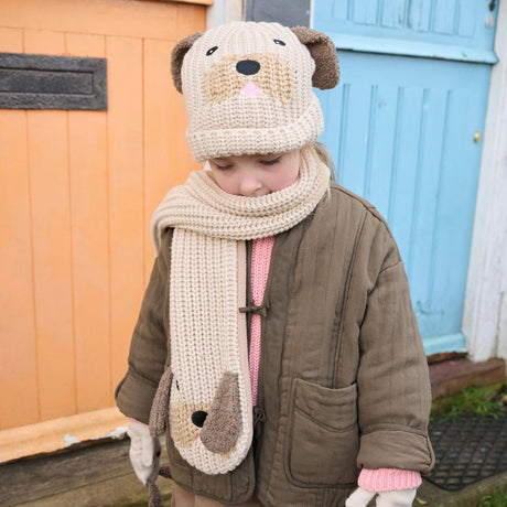 Kind buiten met beige gebreide puppymuts met bruine oortjes, bijpassende sjaal en bruine jas