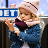 Kind met roze Sunshine-muts, roze en pruimkleurige sjaal en een spijkerjas.