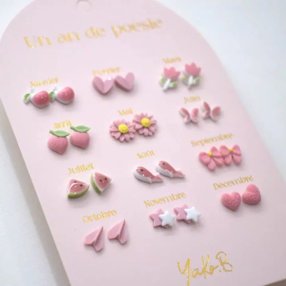 Twaalf paar oorbellen in roze thema op een roze kaart, met onder meer hartjes, bloemen, aardbeien en sterren.