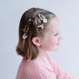 Meisje in zijaanzicht met paarden- en bloemenhaarclips naast een vlecht en een roze vest.