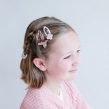 Meisje met een roze paardenhaarclip en een lichte bloemenhaarclip naast een vlecht in haar bruine haar.