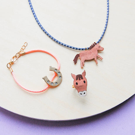 Paardenjuwelenset met blauw-witte ketting met paardje, roze armband met glinsterend hoefijzer en paardenring.