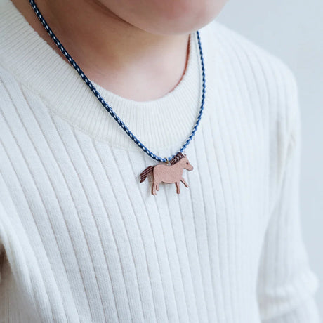 Detail van een blauw-witte ketting met bruin paardje, gedragen op een witte geribde trui.