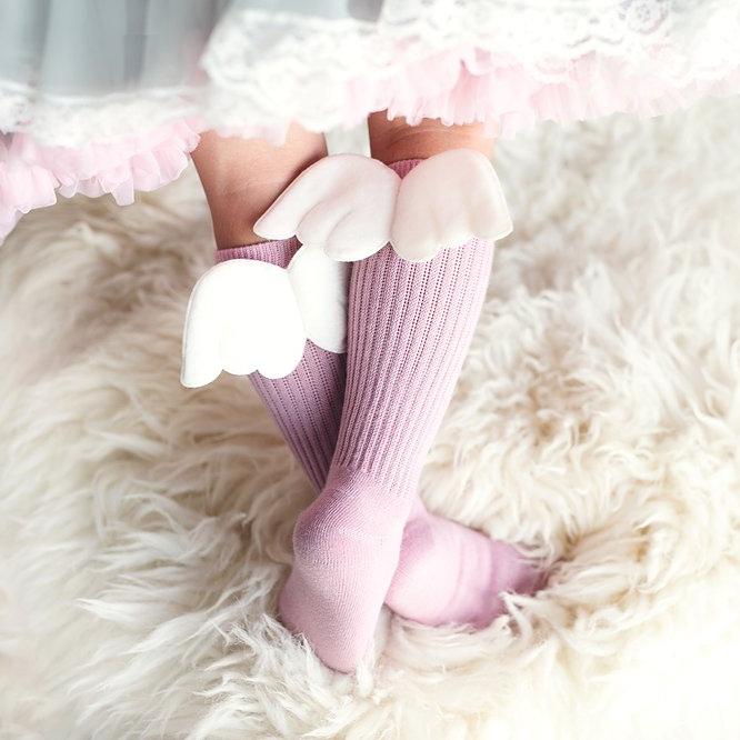 Kind draagt roze kniekousen met witte vleugeltjes onder een rok met wit kant en roze ruches.