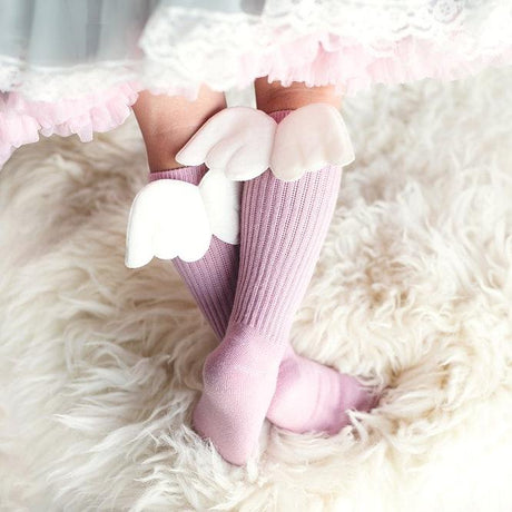Kind draagt roze kniekousen met witte vleugeltjes onder een rok met wit kant en roze ruches.