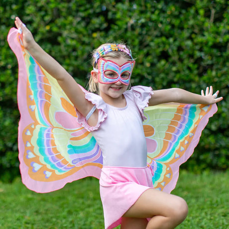 Kind met kleurrijke vlindervleugels en roze vlindermasker, met gespreide armen in de tuin