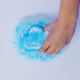 Een hand houdt de blauwe regenboogbruisbal in wolkvorm in het badwater, omringd door blauwe bubbels.