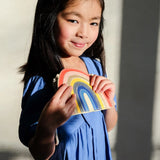 Meisje in een blauwe jurk met het regenboogtasje van Mimi & Lula in rood, geel en blauw.