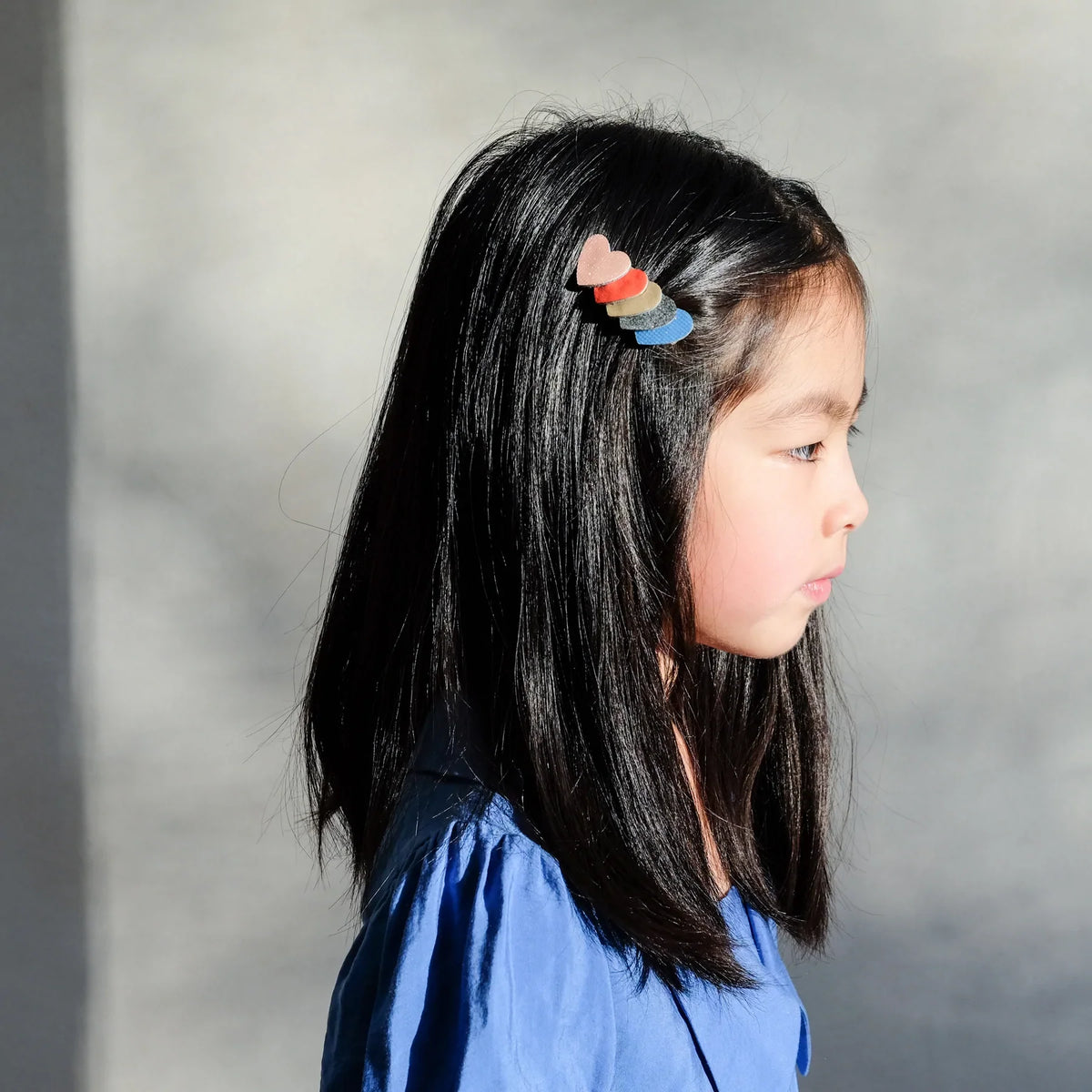 Meisje met een Retro Rainbow haarspeldje met gelaagde hartjes in roze, rood, goud en blauw in donker haar.