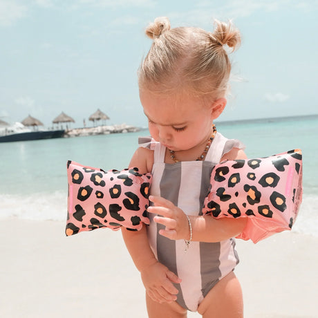 Kind met rosékleurige zwembandjes met panterprint en een gestreept badpak op het strand.