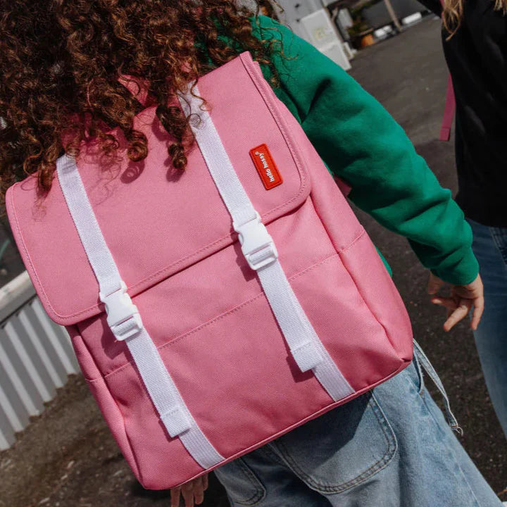 Roze Hello Hossy Mini Taffy rugzak met witte sluitriemen, gedragen door een kind in een groene trui.
