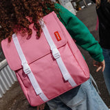 Roze Hello Hossy Mini Taffy rugzak met witte sluitriemen, gedragen door een kind in een groene trui.