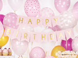 Roze Happy Birthday-slinger met gouden letters tussen roze, witte en gouden ballonnen boven een feesttafel.