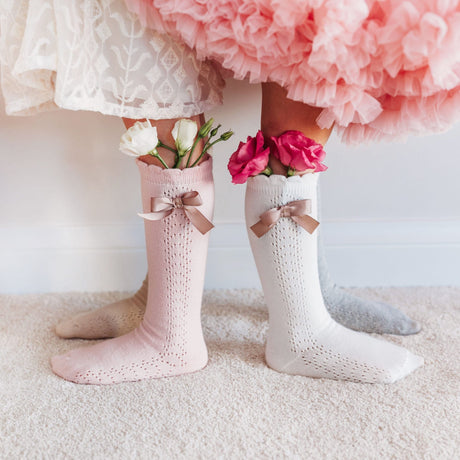 Roze, witte en grijze kniekousen met strikjes, gedragen door kinderen, met bloemen in de boorden.