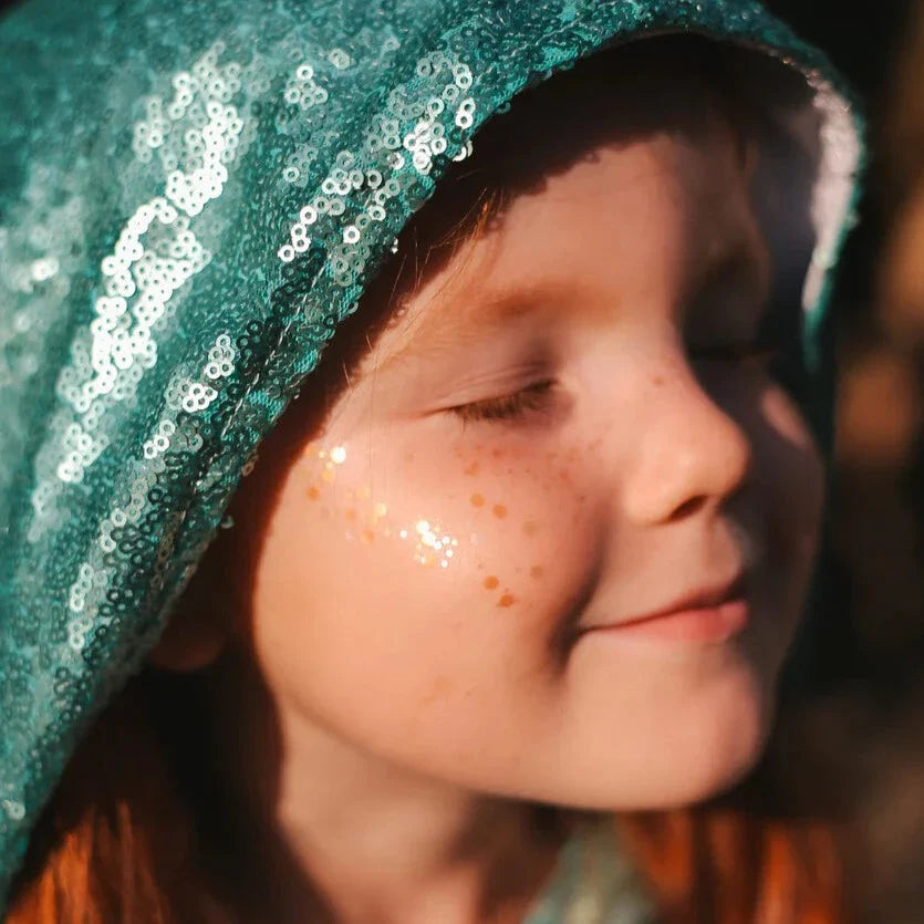 Gouden gezichtsglitter op de wang van een kind met een groene capuchon vol pailletten.