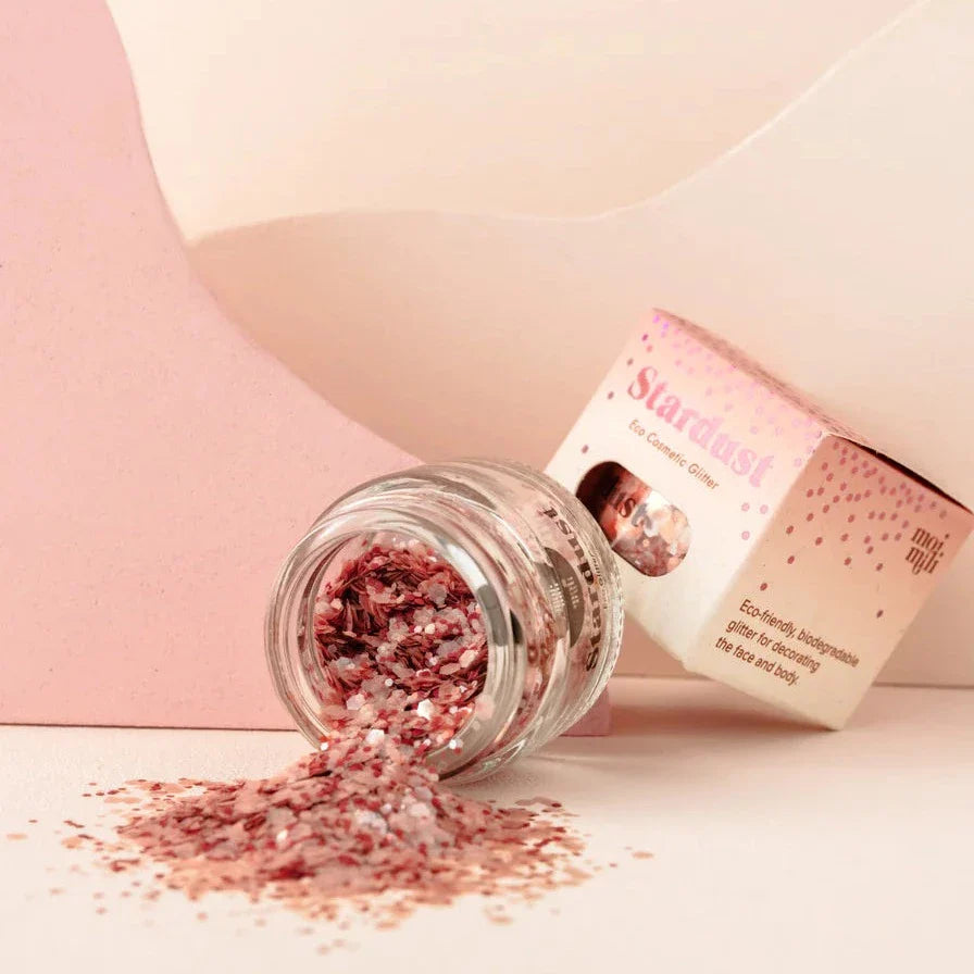 Star Dust Pink Star gezichtsglitter in een gekanteld glazen potje, met uitgestrooide roze glitter en verpakking erachter