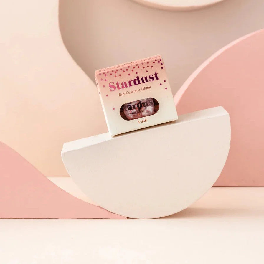 Verpakking van Star Dust Pink Star gezichtsglitter op een halfrond blok tegen een roze achtergrond