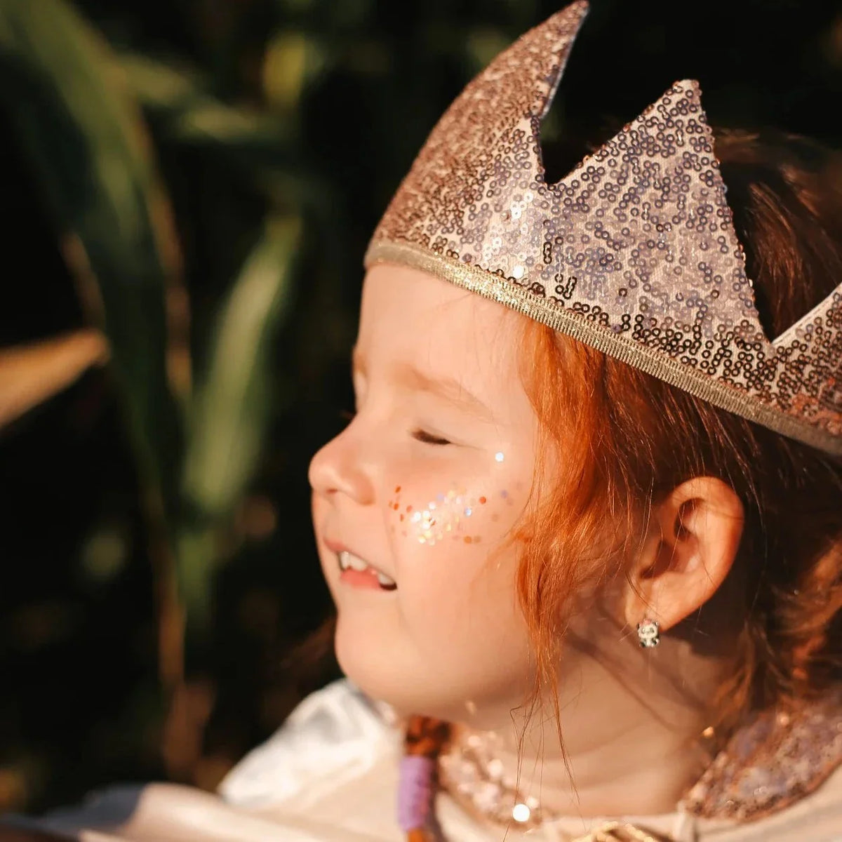 Kind met een glinsterende kroon en Star Dust Rainbow gezichtsglitter in verschillende kleuren op de wang.