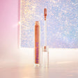 Stardust Topper Camille in een transparant flesje met applicator en koperkleurige glans, tegen een glinsterende achtergrond.