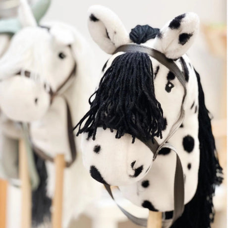 Wit stokpaardje met zwarte stippen, zwarte manen en bruin hoofdstel, naast een wit stokpaardje.