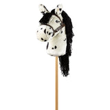 Wit stokpaardje met zwarte stippen, lange zwarte manen en een bruin hoofdstel, schuin van voren gezien.