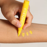 Hand tekent met een gele tattoopen op een onderarm, naast drie gele kleurstrepen.