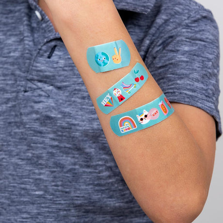 Drie turquoise Top Banana pleisters met kleurrijke figuurtjes in verschillende formaten op een arm.
