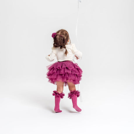 Kind van achteren met het roze Tutu Bloomer Heather Pink rokje, een witte trui en roze kniekousen.