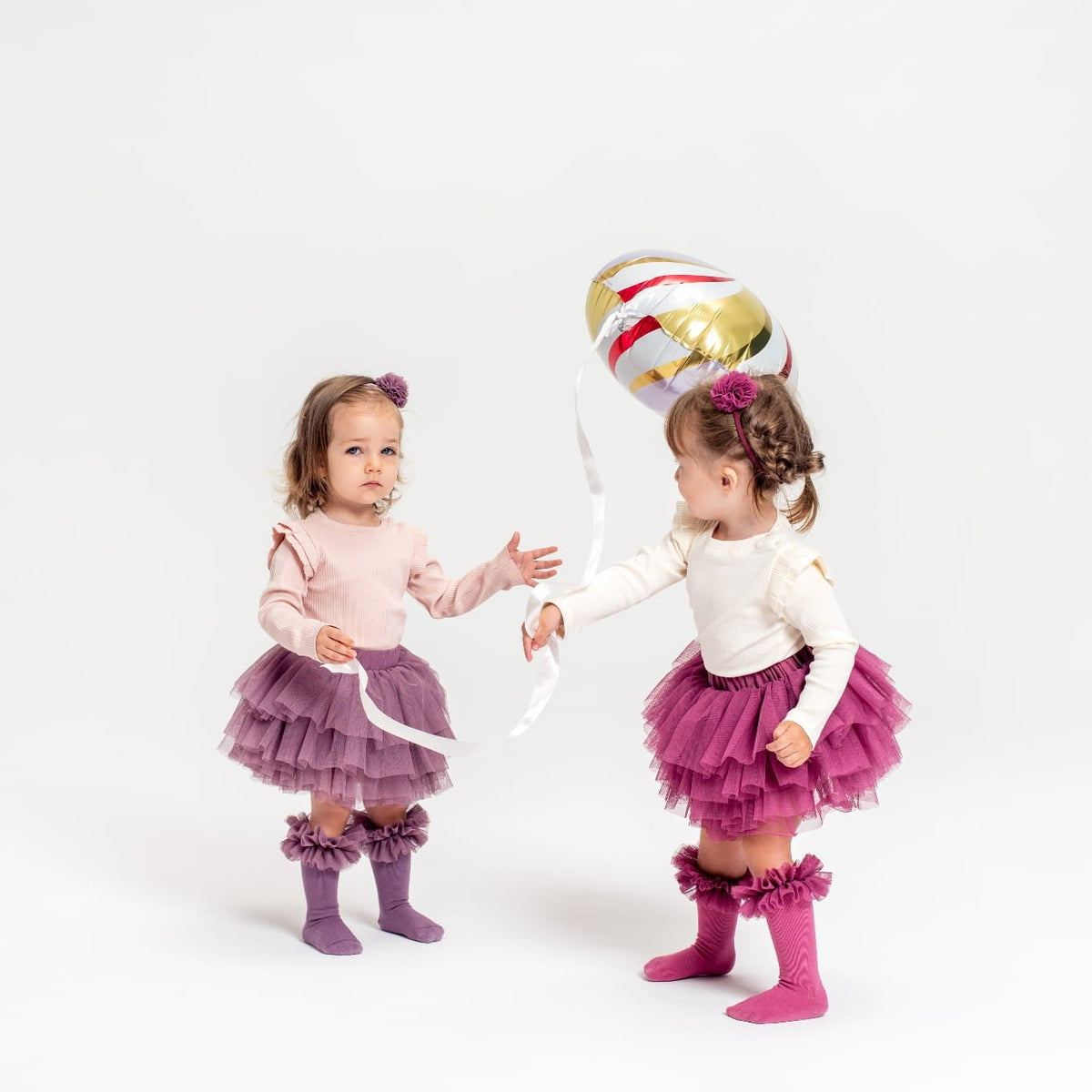 Twee kinderen met tutu rokjes in paars en roze, bij een ballon; rechts het Tutu Bloomer Heather Pink rokje.