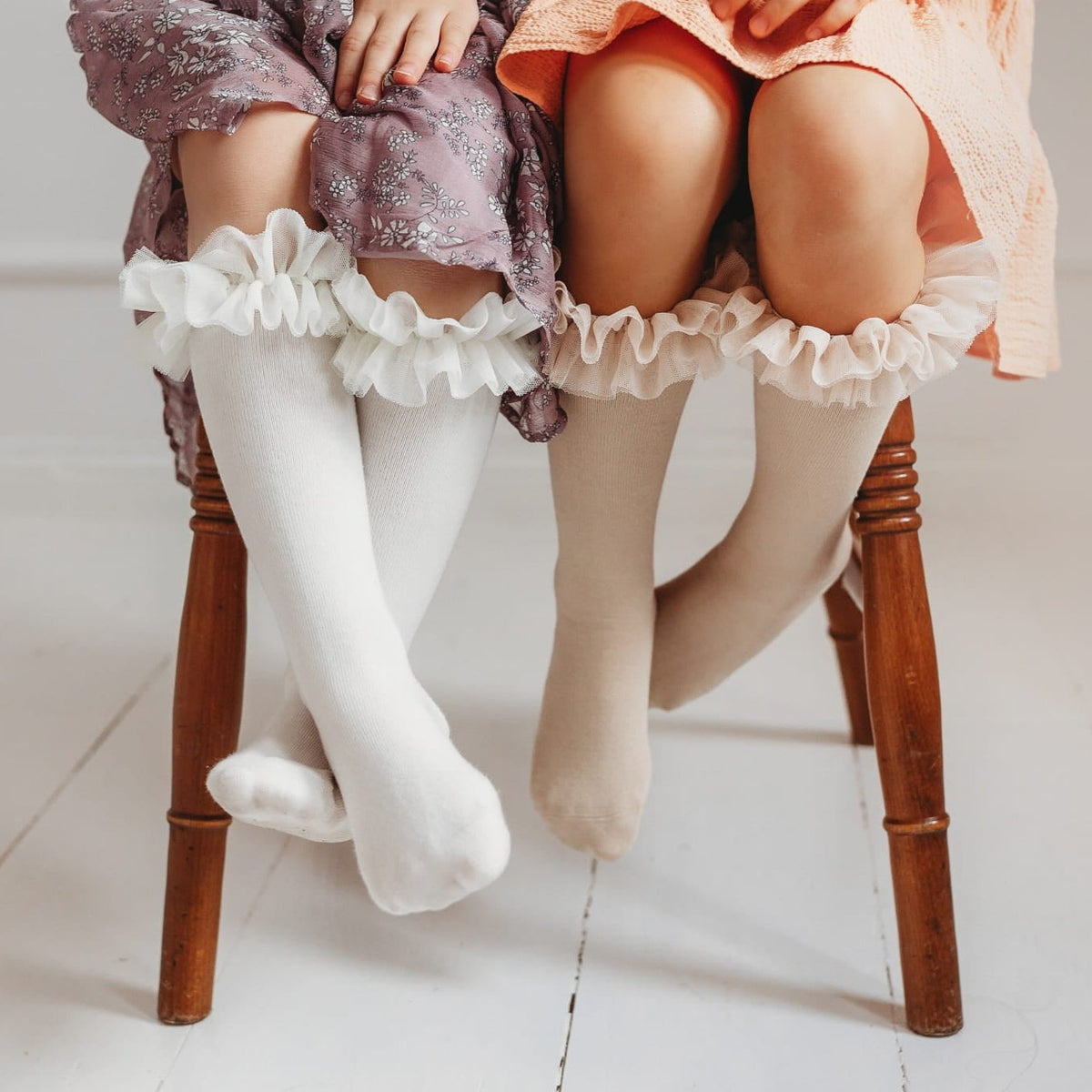 Close-up van twee kinderen op een houten stoel met witte en beige tutu kniekousen met ruches.