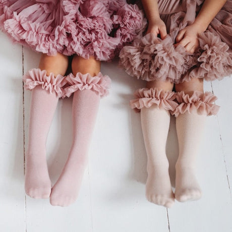 Twee kinderen met roze en lichtgekleurde tutu kniekousen met ruches, onder bijpassende rokken.