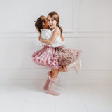 Twee kinderen omhelzen elkaar in tutu rokken en kniekousen met ruches, één in oudroze en één in een lichte tint.