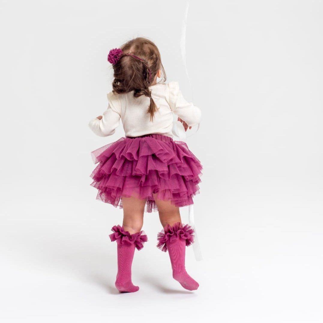 Kind van achteren met roze tutu kniekousen met ruches, een roze rok en een witte trui.