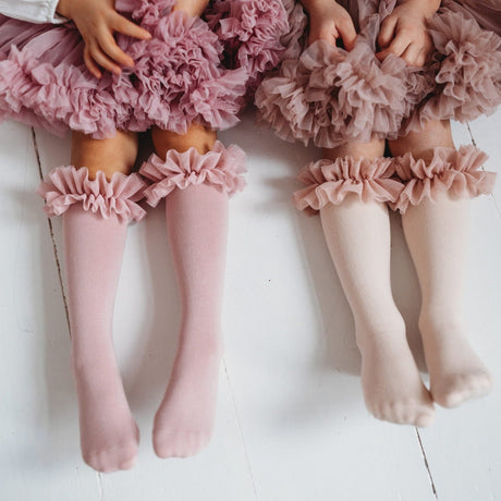 Roze en lichtroze tutu kniekousen met ruches, gedragen door twee kinderen met bijpassende rokken.