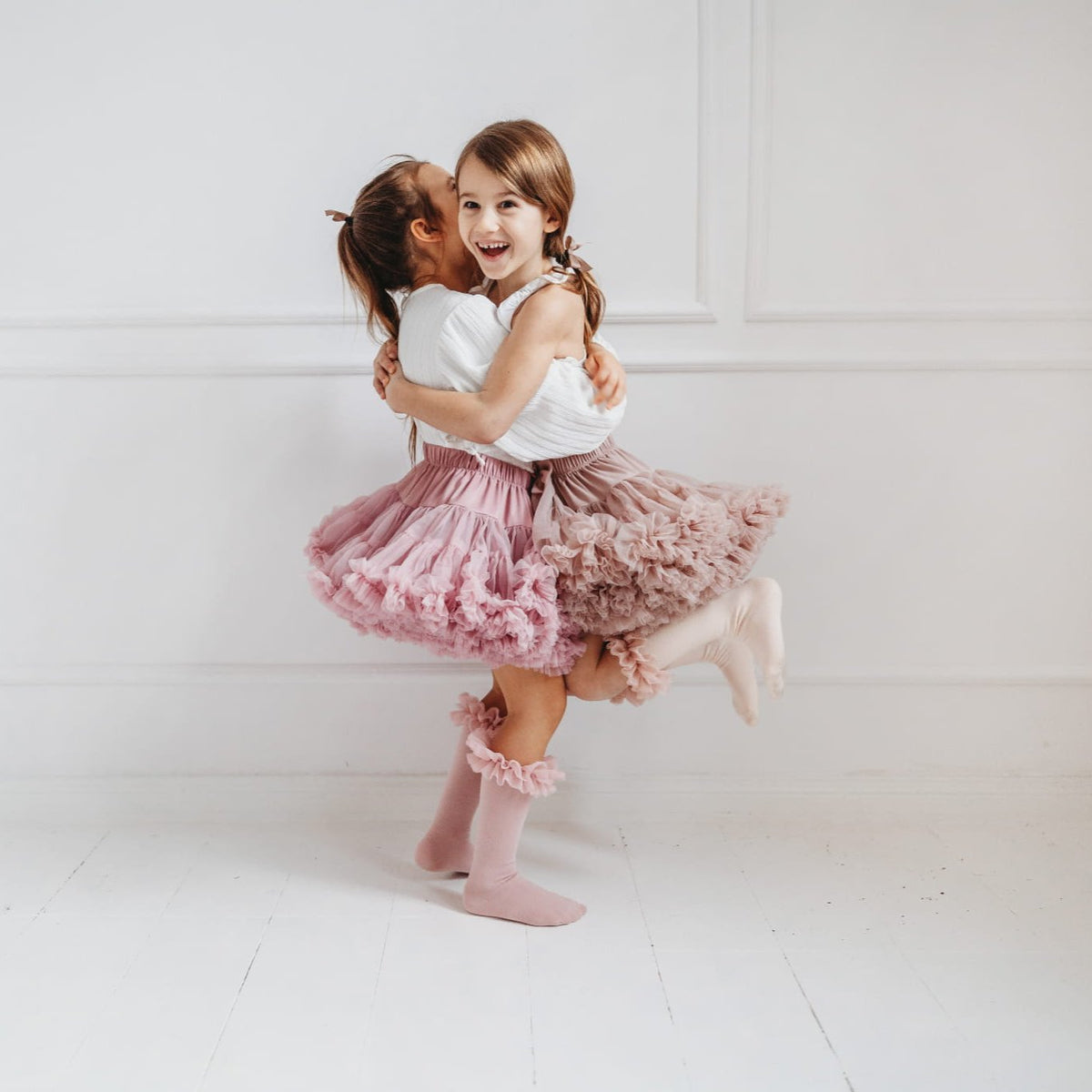 Twee kinderen omhelzen elkaar in tutu rokken en roze en lichtroze kniekousen met ruches.