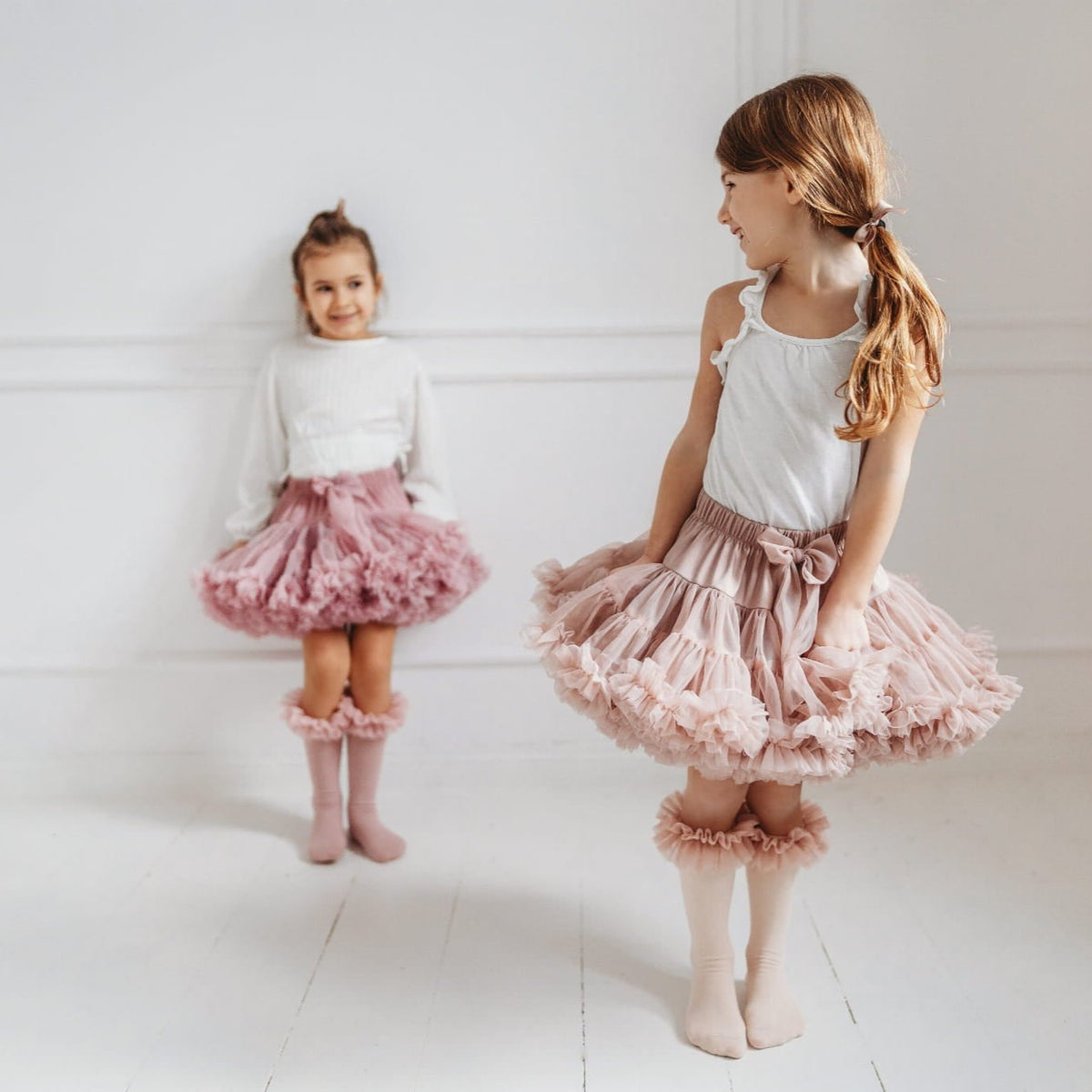 Kind met lichtroze tutu kniekousen en een bijpassende rok, met een tweede kind in roze op de achtergrond.