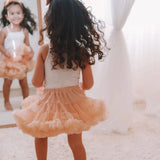 Achteraanzicht van een meisje in de perzikkleurige Loli tutu rok en een witte top voor een spiegel.
