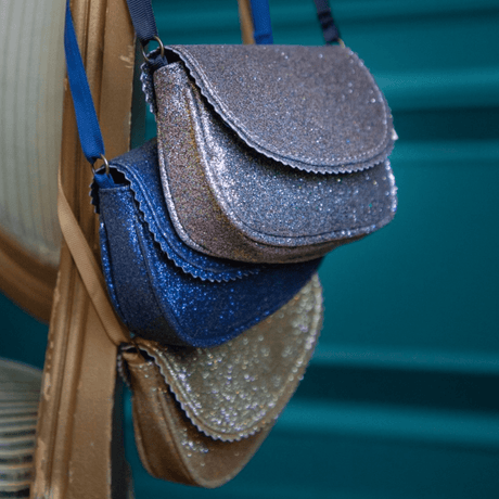 Lavendelkleurige Urfa schoudertas met glitters, hangend boven een blauwe en goudkleurige glittertas.