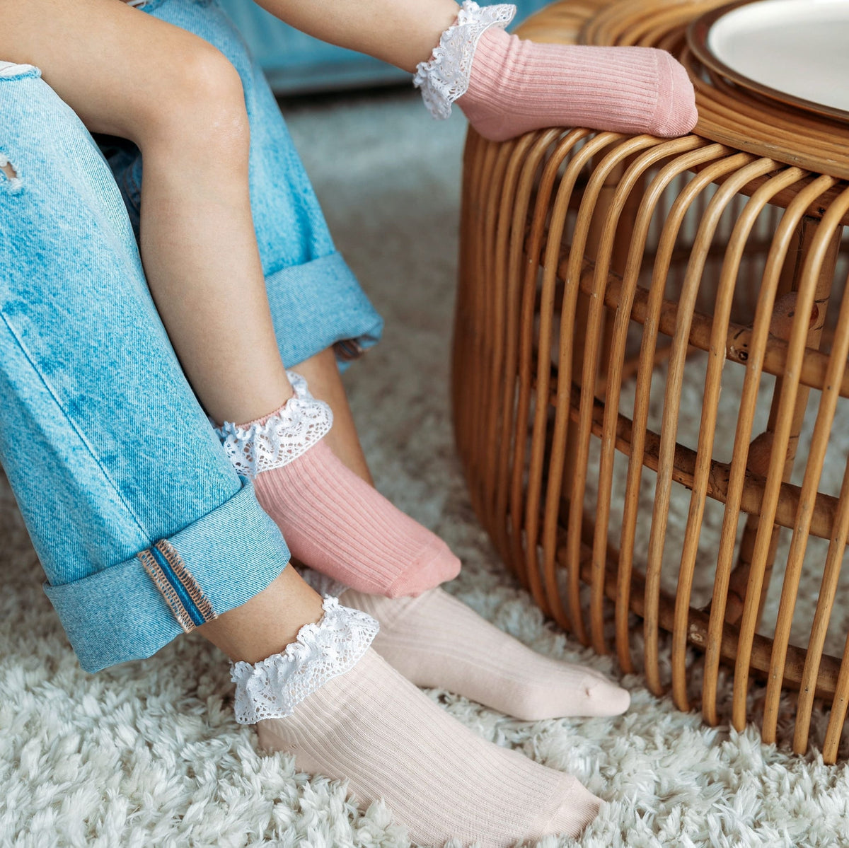 Licht abrikooskleurige en roze sokken met witte kanten ruches, gedragen bij jeans naast een rotan tafel.