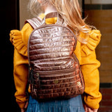 Walker rugtas in Dark Gold op de rug van een kind, met horizontale stiksels en een voorvak met rits.