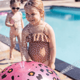 Kinderen spelen bij de roze watersproeier met panterprint en waterstralen aan de rand van het zwembad.