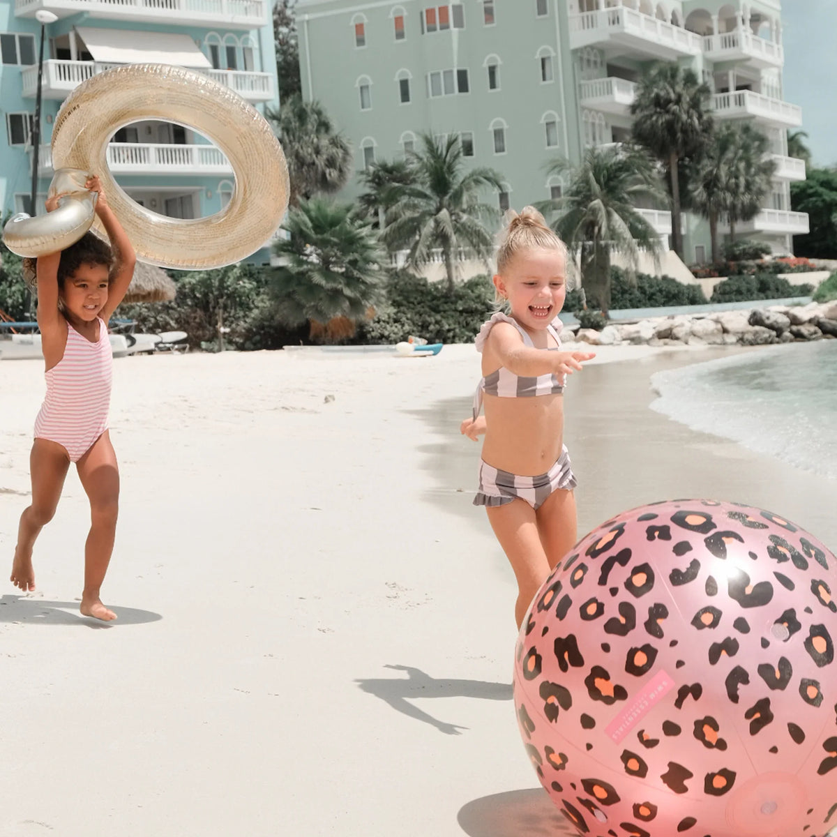 Kinderen spelen op het strand met een roze watersproeier met panterprint en een zwemband.