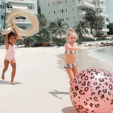 Kinderen spelen op het strand met een roze watersproeier met panterprint en een zwemband.
