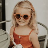 Kind met de Kidooz Apricot zonnebril op, zittend aan tafel met een ijsje.