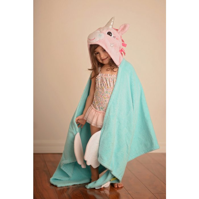 Kind draagt de turquoise Allie the Alicorn badcape met roze eenhoorncapuchon en witte vleugels binnenshuis.